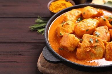 Photo of Delicious chicken curry in pan on wooden table, closeup. Space for text