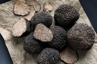 Photo of Whole and cut black truffles on parchment, top view