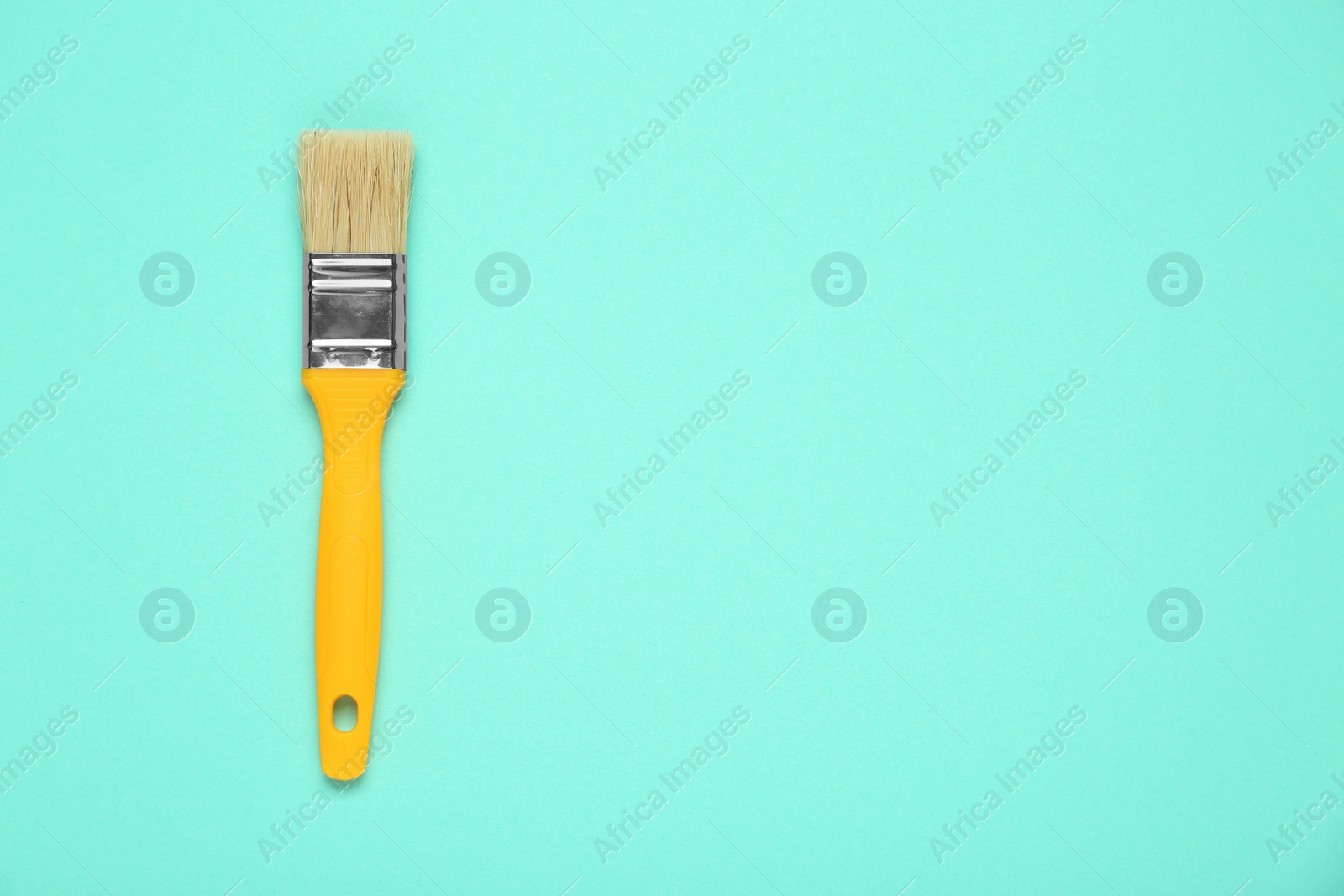 Photo of One paint brush with yellow handle on turquoise background, top view. Space for text
