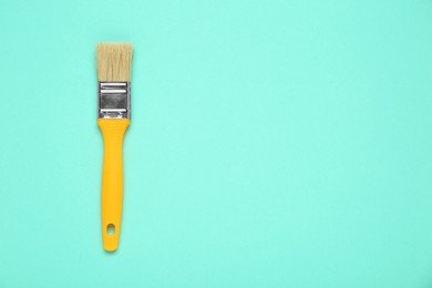 One paint brush with yellow handle on turquoise background, top view. Space for text