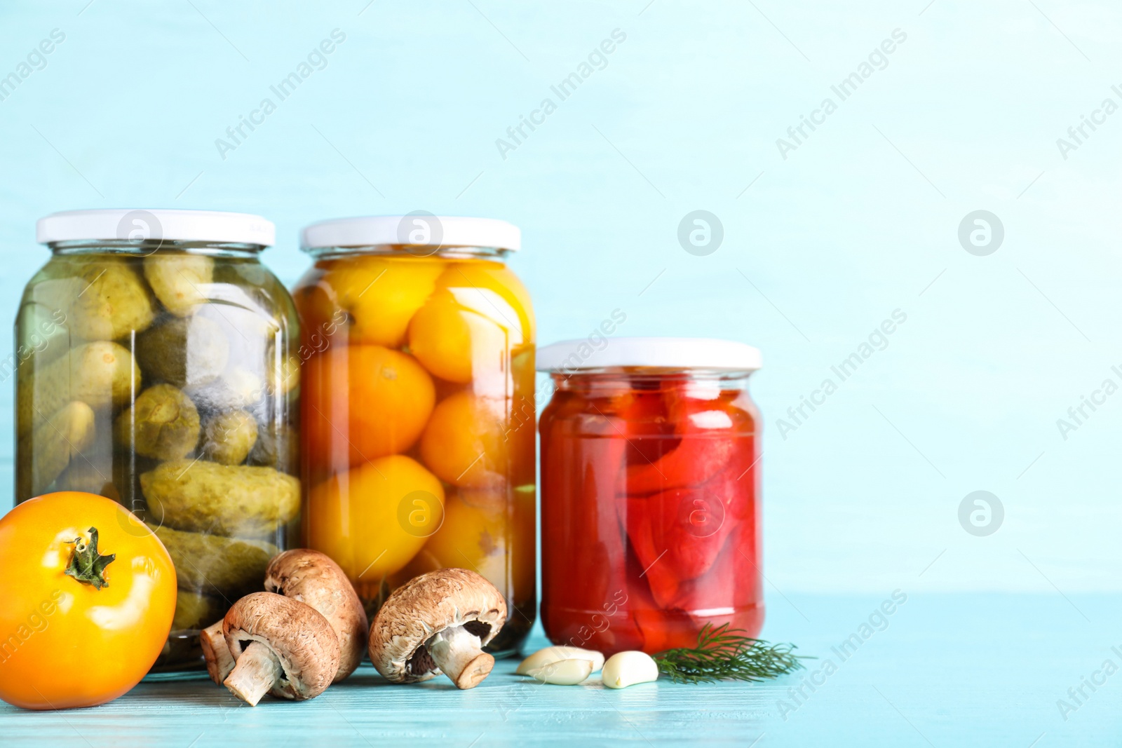 Photo of Glass jars with different pickled vegetables on light blue wooden table. Space for text