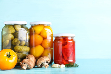 Photo of Glass jars with different pickled vegetables on light blue wooden table. Space for text