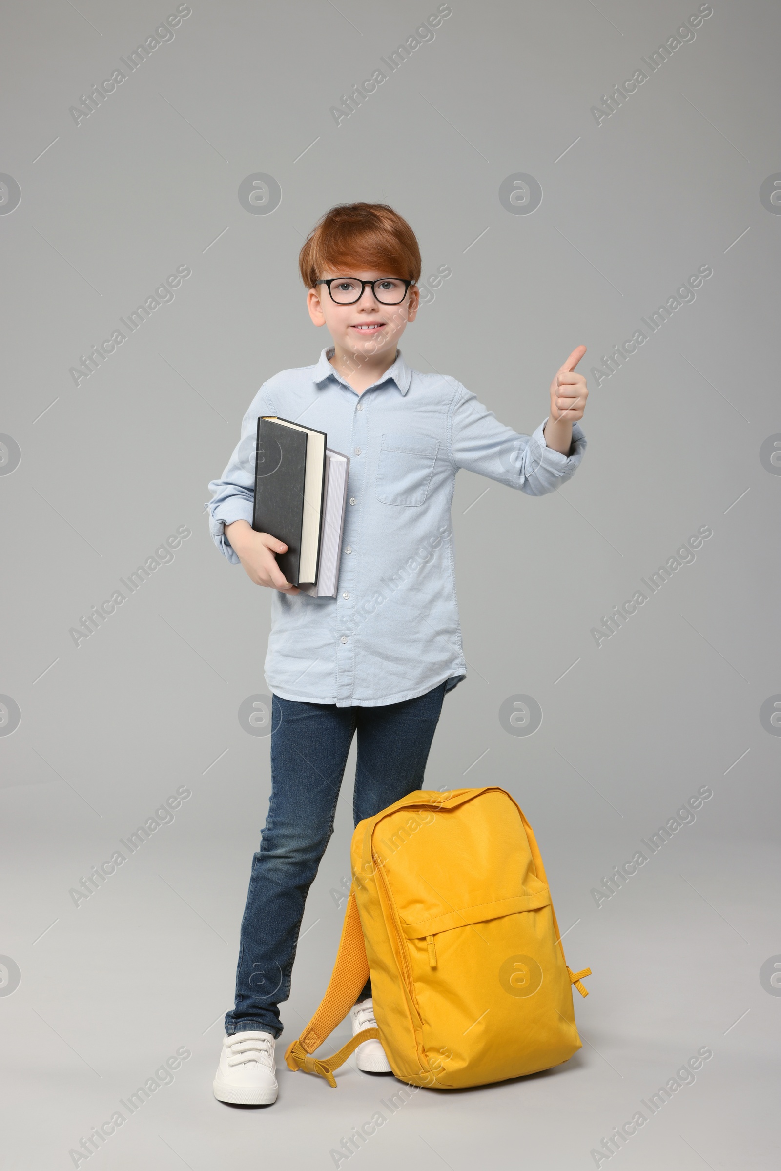 Photo of Happy schoolboy with books showing thumb up on grey background