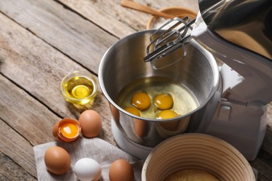 Photo of Making dough. Raw eggs in bowl of stand mixer and ingredients on wooden table
