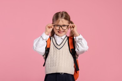 Photo of Happy schoolgirl in glasses with backpack on pink background
