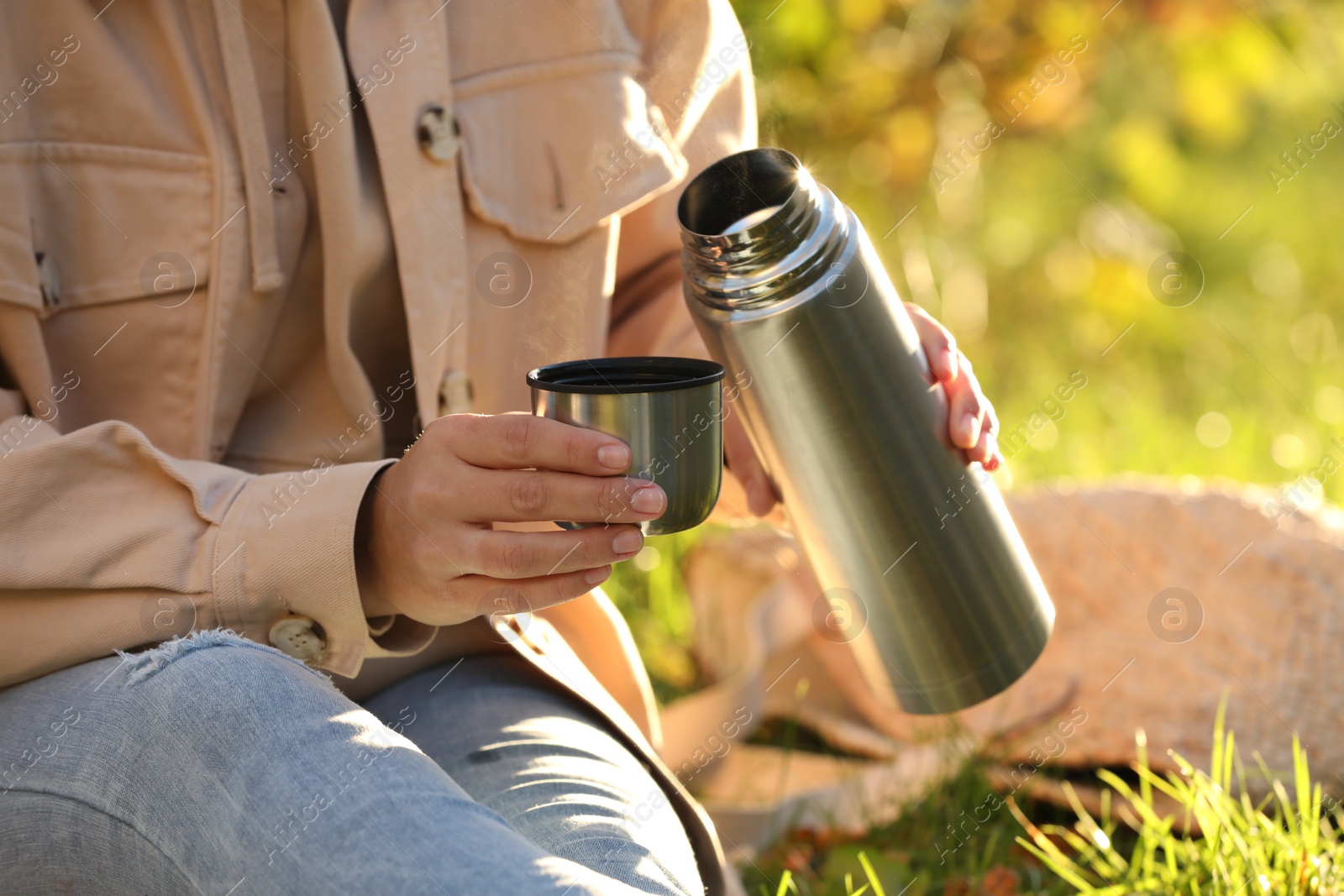 Photo of Picnic time. Woman with thermos and cup lid on green grass outdoors, closeup