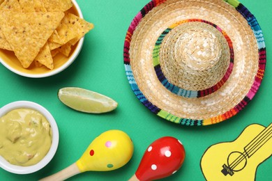 Mexican sombrero hat, nachos chips, guacamole, maracas, lime and paper guitar on green background, flat lay