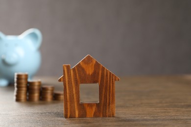 House model, piggy bank and stacked coins on wooden table, selective focus. Space for text