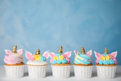 Photo of Many cute sweet unicorn cupcakes on white wooden table against light blue background