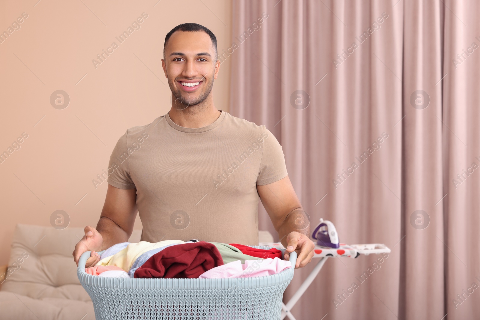 Photo of Happy man with basket full of laundry at home