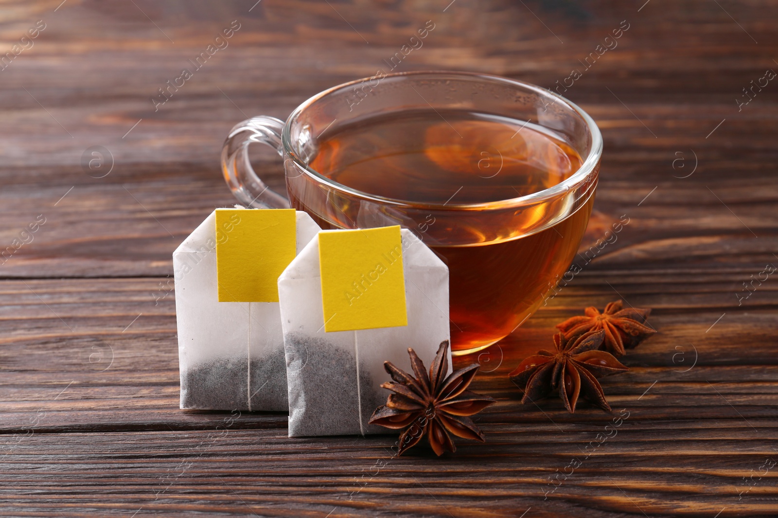 Photo of Tea bags, cup of hot drink and anise stars on wooden table, closeup