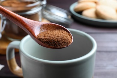 Spoon of instant coffee over mug on wooden table, closeup