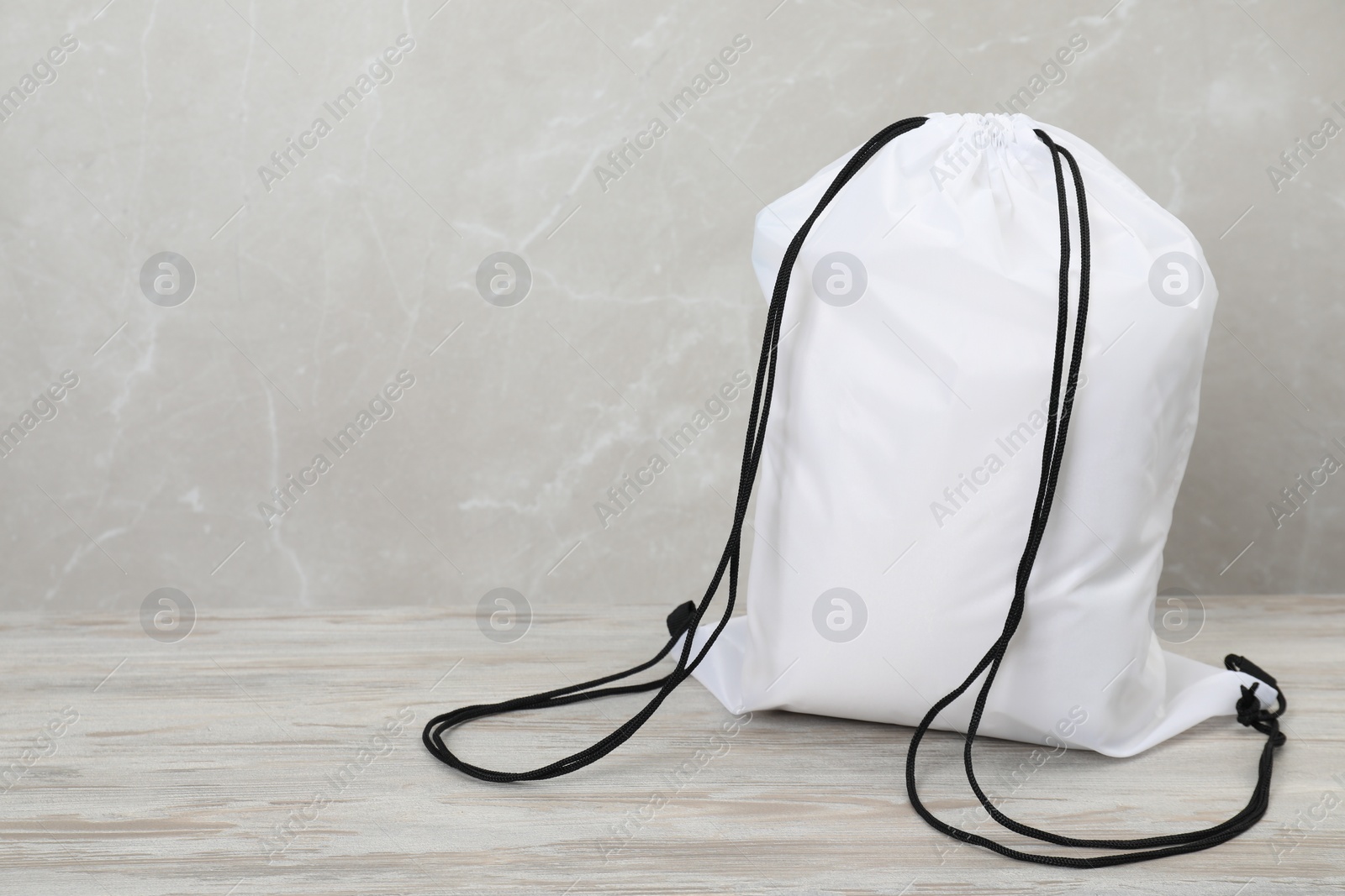 Photo of White drawstring bag on light wooden table. Space for text