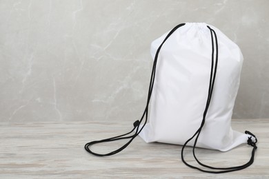 Photo of White drawstring bag on light wooden table. Space for text