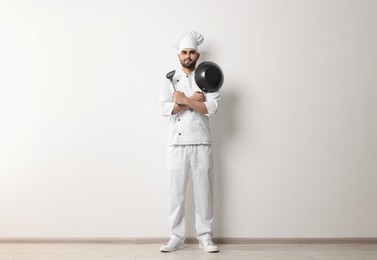 Photo of Professional chef with wok and spatula near white wall indoors