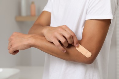 Photo of Man putting sticking plaster onto elbow indoors, closeup