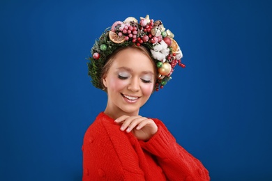 Beautiful young woman wearing Christmas wreath on blue background