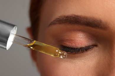 Photo of Beautiful young woman applying cosmetic serum onto her face on grey background, closeup