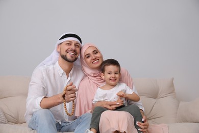 Happy Muslim family spending time together on sofa at home, space for text
