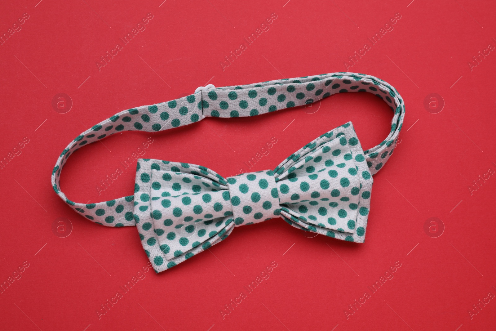 Photo of Stylish white bow tie with green polka dot pattern on red background, top view