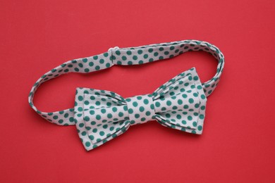 Photo of Stylish white bow tie with green polka dot pattern on red background, top view