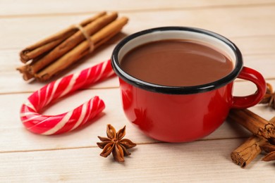 Tasty hot chocolate, candy cane and spices on light wooden table, closeup