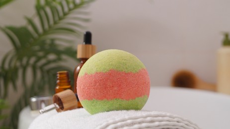 Photo of Towel with bath bomb and bottles of essential oils on tub indoors, closeup
