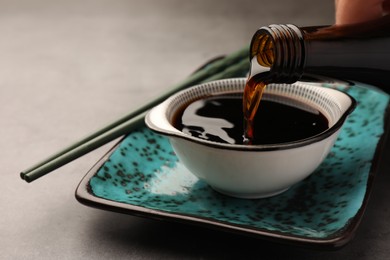 Photo of Pouring soy sauce into bowl on grey table, closeup