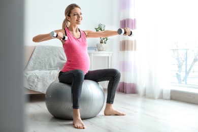 Photo of Young pregnant woman doing exercises with dumbbells at home