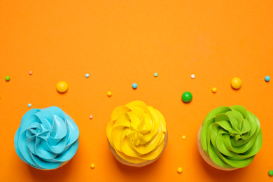 Photo of Colorful birthday cupcakes on orange background, flat lay. Space for text