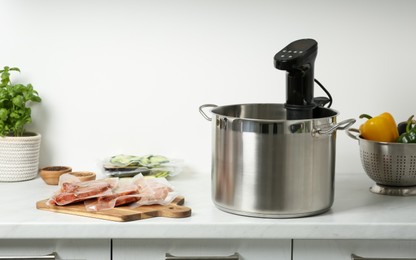 Photo of Thermal immersion circulator in pot and vacuum packed food products on countertop in kitchen. Sous vide cooking