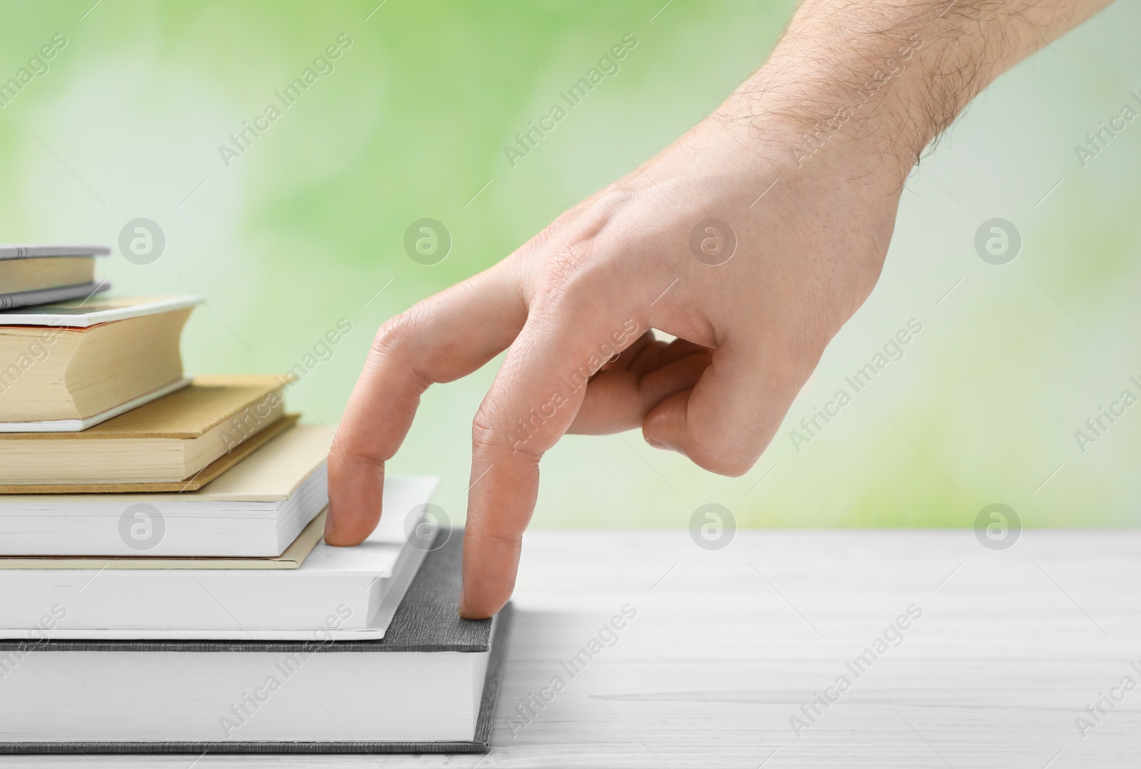 Photo of Man climbing up stairs of books with fingers on white wooden table against blurred background, closeup