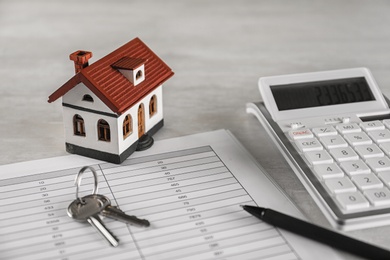 Calculator, house model, keys and documents on light table. Real estate agent's workplace