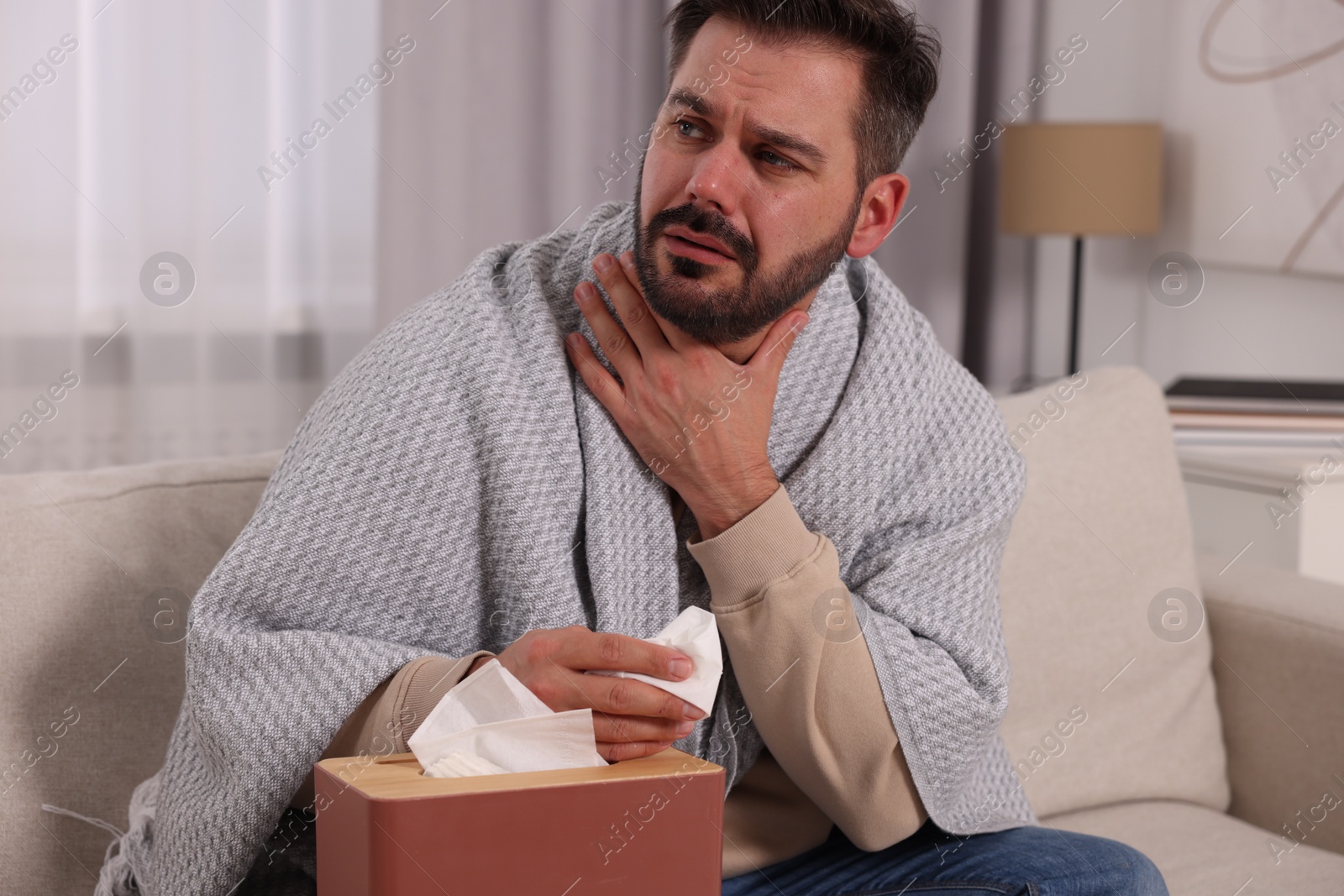 Photo of Sick man wrapped in blanket with tissues on sofa at home. Cold symptoms