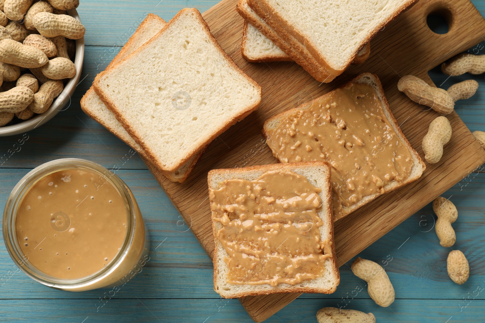 Photo of Delicious toasts with peanut butter and nuts on light blue wooden table, flat lay