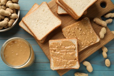 Delicious toasts with peanut butter and nuts on light blue wooden table, flat lay