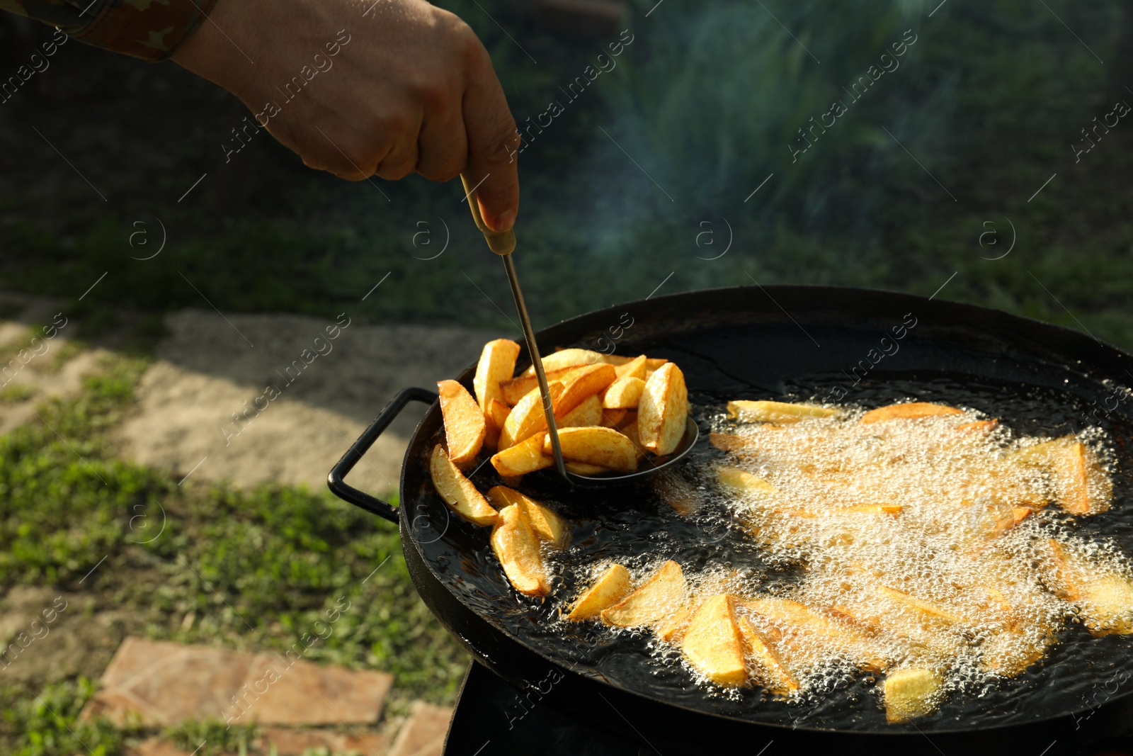 Photo of Man cooking delicious potato wedges on frying pan outdoors, closeup