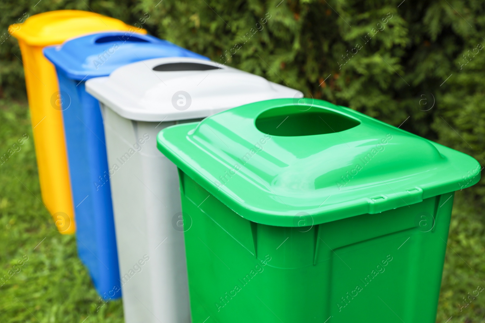 Photo of Many color recycling bins on green grass outdoors, closeup