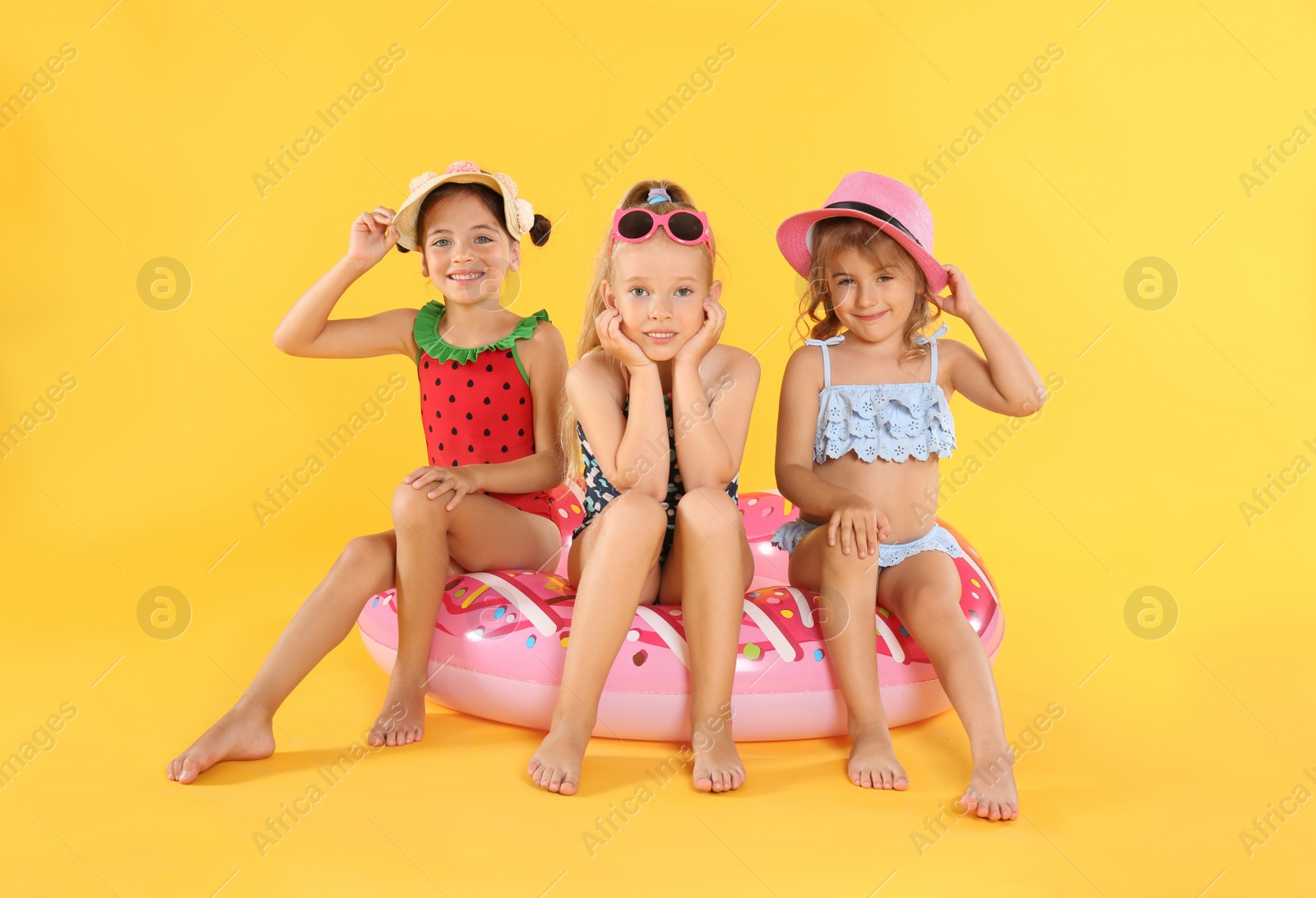 Photo of Cute little children in beachwear with bright inflatable ring on yellow background