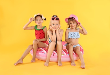 Photo of Cute little children in beachwear with bright inflatable ring on yellow background