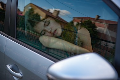 Photo of Tired girl sleeping in car, view from outside
