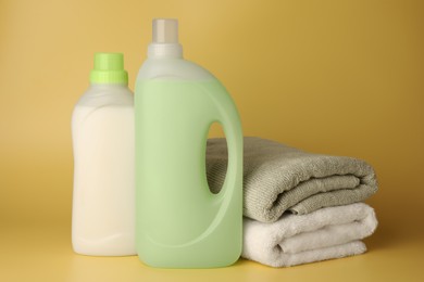 Photo of Bottles of fabric softener and stacked clean towels on pale yellow background