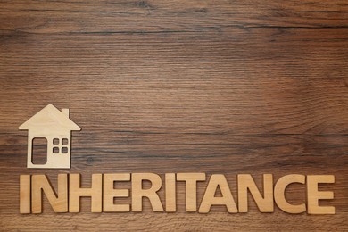 Photo of Word Inheritance made with letters and house model on wooden background, flat lay. Space for text