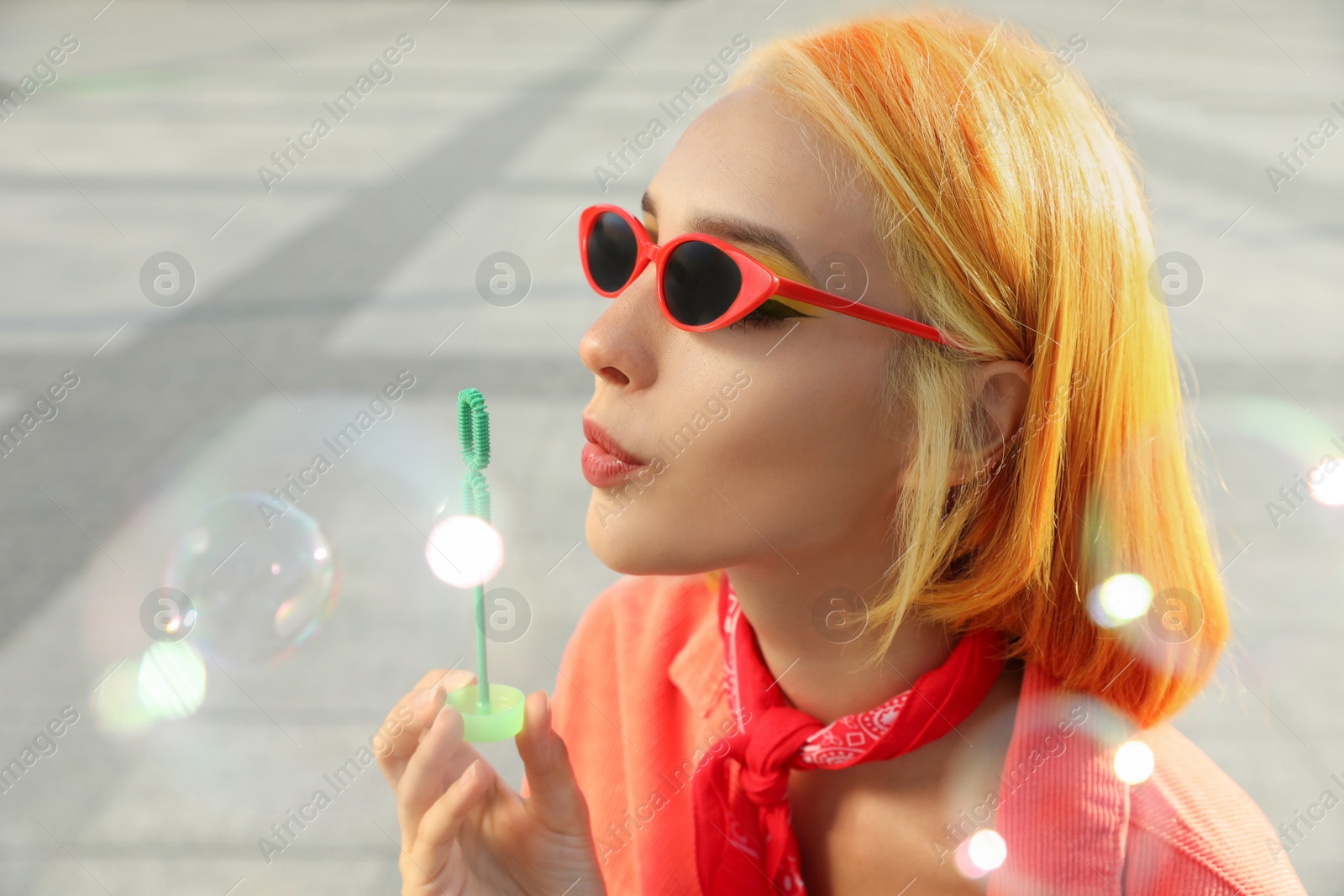 Photo of Beautiful young woman with bright dyed hair blowing soap bubbles outdoors