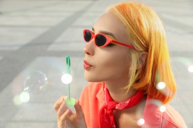 Beautiful young woman with bright dyed hair blowing soap bubbles outdoors