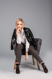 Photo of Young stylish woman with trendy shoes sitting in armchair on grey background