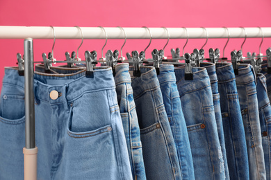 Photo of Rack with stylish jeans on pink background, closeup