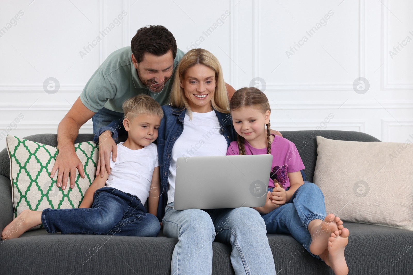 Photo of Happy family with laptop spending time together on sofa at home