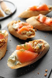 Photo of Tasty bruschettas with salmon and blue cheese on slate plate, closeup