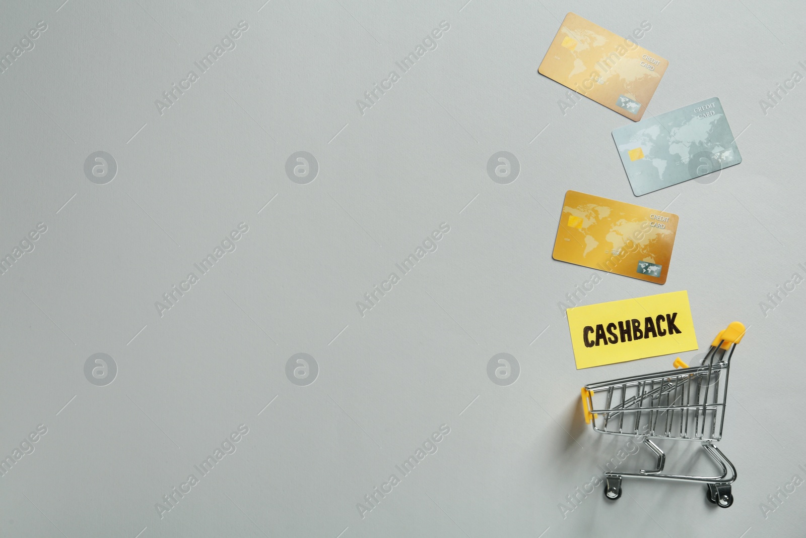 Photo of Shopping cart and different credit cards on light grey background, flat lay with space for text. Cashback concept